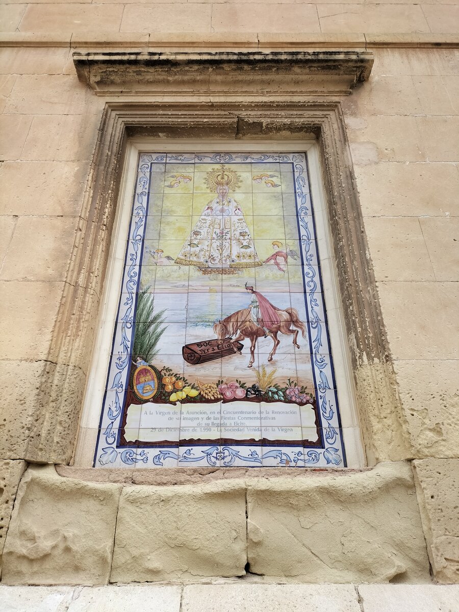 Elche, Wandbild Virgen de la Asuncin bei der Basilica de Santa Maria, am 07.10.2024. Im Jahr 1370 strandete eine Holzkiste mit dem Bild von Mari Himmelfahrt in der Nhe von Elche am Mittelmeer. Der damalige Offizier der Kstenwache Francesc Cant endeckte die Reliquie.