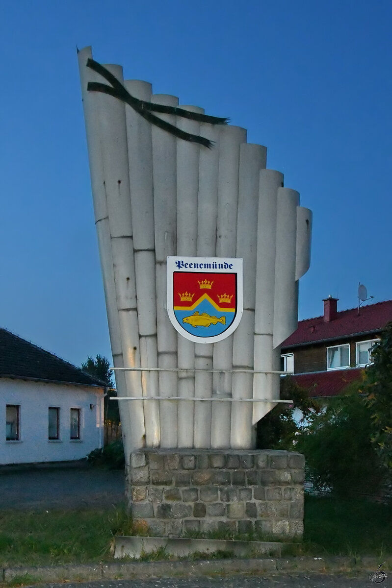 Im Bild das 1996 entstandene Wappen der Gemeinde Peenemnde mit den drei Kronen zur Erinnerung an die Landung der schwedischen Flotte und den Beginn der schwedischen Herrschaft in Vorpommern. Der gebrochene Faden steht als Symbol fr die Peenemndung in die Ostsee und der Fisch fr die Fischwirtschaft. (Peenemnde, September 2024)