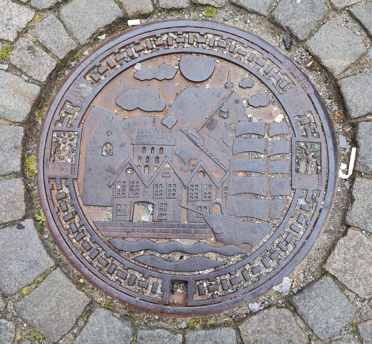 Kanaldeckel der Stadt Bergen/Norwegen. Dargestellt ist durch das Segelschiff der Hafen, das Hanseviertel Bryggen, die Floi- und die Ulrike-Bahn, und die Festung Bergenhus, 09-2024