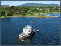 Die winzige Insel Dyna an der Einfahrt zum Hafen Oslo wurde 1874 mit einem Leuchtfeuer bebaut. Heute dient das Geb�ude als Restaurant. Dahinter befindet sich die zu Oslo geh�rende Halbinsel Bygd�y. Im Hintergrund ist die Skischanze Holmenkollbakken zu erkennen. (Oslo, 28.05.2023)