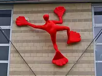 Roter Flossi auf dem Weg nach oben. Dieser poppige Kletterer der Objektk�nstlerin Rosalie erklimmt das Institut f�r Kunststoffverarbeitung (IKV) an der RWTH Aachen am Seffenter Weg. Die Figur ist von 2005, aus Glasfaserverst�rktem Kunststoff, mit Acryl Lackiert und ca. 3,2 mal 2,0 Meter gro�. Die K�nstlerin Rosalie ist unter anderem auch Malerin, B�hnenbildnerin und Professorin f�r Gestaltung an der Hochschule Offenbach.