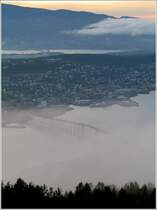 Neblige Ansicht von Troms�: Vorne die bekannte Br�cke, in der Mitte die Insel, auf der der gr��te Teil der bebauten Stadt liegt. Dahinter die Insel Kval�ya, zu der eine weitere im Bild erkennbare Br�cke f�hrt. 10.8.2006 (Jonas)