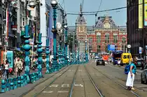 Amsterdam -  Damrak , Gesch�ftsstra�e und im Hintergrund der Bahnhof. Die Dame rechts unten im Bild hat Ihr T-Shirt farblich passend zu den  Skulpturen  am linken Strassenrand angepa�t - 23.07.2013