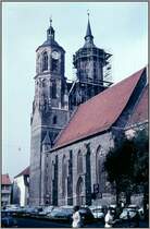 Die St. Johanniskirche in G�ttingen, aufgenommen etwa Anfang der 60er Jahre des vergangenen Jahrhunderts. Das Bild ist der Scan eines Dias aus dem Archiv meines Vaters Alfred Schmidt. Die Kirche wurde von 1300 bis 1344 gebaut. Ihre T�rme geh�ren zu den Wahrzeichen der Stadt. Meine Familie und ich haben lange Zeit nur wenige hundert Meter von dieser Kirche entfernt in der Johannisstra�e gewohnt. Wie man sehen kann wurde zu dieser Zeit der Platz um die Kirche herum noch als Parkplatz genutzt. Einer der T�rme wurde saniert. Im R�cken des Fotografen befindet sich das alte Rathaus der Stadt.