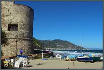 Der aus dem 16. Jahrhundert stammende Torrione del Cavallo, eines der Wahrzeichen des K�stenortes Laigueglia, wacht �ber die auf dem Strand liegenden, bunten Fischerboote. Im Hintergrund ist die Stadt Alassio zu sehen, die unmittelbar n�rdlich von Laigueglia liegt. (25.09.2018)