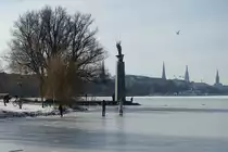 Hamburg-Hohenfelde am 14.2.2021: Blick auf die Alsterwiese Schwanenwik mit dem Denkmal „Drei M�nner im Boot“, weiterhin die sorglosen Mitb�rger auf dem nicht freigegebenen Eis der Alster /