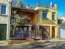 Dieses Foto habe ich in P�cs, in der Stadtteil  Erzs�bettelep  (Elisabethsiedlung) gemacht. Dieser Stadteil wurde durch die Donaudampfschiffgesellschaft gegr�ndet. Die  Kolonie  stand aus 4 Strassen und 32 H�user. Es gab 6 kleine Wohnungen pro Haus zzgl Gartenteil und Nebengeb�ude. Vor ca. 100-120 Jahren wurden neue Kohlenminien in der N�he er�ffnet und die dort arbeitenden haben hier Wohnungen bekommen. Die Siedlung hie� urspr�nglich Ullmannsiedlung, genannt nach einem Leiter des Unternehmens. 1938 wurde auf Elisabethsiedlung umbenannt (von Elisabeth Amalie Eugenie von Wittelsbach K�nigin genannt). Die H�user waren �berdurchschnittlich ausger�stet, da Leitungswasser und Strom auch vorhanden war. In den vergangenen guten Jahrhundert wurde es nicht geregelt wie man die Geb�uden/Wohnungen �ndern, erweitern, umbauen oder zusammenlegen/vereinigen darf. Deswegen ist auf heutzutage das Strassenbild ganz ganz gemischt (und daher meiner Meinung nach, sehr einzigartig und interessant) geworden. Die Etagen wurden ge�ndert, Dachgeschosse wurden eingebaut...daher findet man hier keine zwei gleiche H�user. Die gro�e �nderungen sind um ca 1926 begonnen. Wegen der damaligen Wohnungsmangel hat die Stadt 2/3-tel der Siedlung in Miete genommen und hat unter anderem eine Kirche und Schule erbaut und ge�ffnet. Aufnahmezeit: November 2020.
Garage und Flachdach sind sicherlich nachtr�gliche Umbauen.