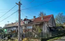 Dieses Foto habe ich in P�cs, in der Stadtteil  Erzs�bettelep  (Elisabethsiedlung) gemacht. Dieser Stadteil wurde durch die Donaudampfschiffgesellschaft gegr�ndet. Die  Kolonie  stand aus 4 Strassen und 32 H�user. Es gab 6 kleine Wohnungen pro Haus zzgl Gartenteil und Nebengeb�ude. Vor ca. 100-120 Jahren wurden neue Kohlenminien in der N�he er�ffnet und die dort arbeitenden haben hier Wohnungen bekommen. Die Siedlung hie� urspr�nglich Ullmannsiedlung, genannt nach einem Leiter des Unternehmens. 1938 wurde auf Elisabethsiedlung umbenannt (von Elisabeth Amalie Eugenie von Wittelsbach K�nigin genannt). Die H�user waren �berdurchschnittlich ausger�stet, da Leitungswasser und Strom auch vorhanden war. In den vergangenen guten Jahrhundert wurde es nicht geregelt wie man die Geb�uden/Wohnungen �ndern, erweitern, umbauen oder zusammenlegen/vereinigen darf. Deswegen ist auf heutzutage das Strassenbild ganz ganz gemischt (und daher meiner Meinung nach, sehr einzigartig und interessant) geworden. Die Etagen wurden ge�ndert, Dachgeschosse wurden eingebaut...daher findet man hier keine zwei gleiche H�user. Die gro�e �nderungen sind um ca 1926 begonnen. Wegen der damaligen Wohnungsmangel hat die Stadt 2/3-tel der Siedlung in Miete genommen und hat unter anderem eine Kirche und Schule erbaut und ge�ffnet. Aufnahmezeit: November 2020. 
Auf diesem Bild lohnt es sich die D�cher anzuschauen. 1Deckung = 1Besitzer = 1 Wohnung